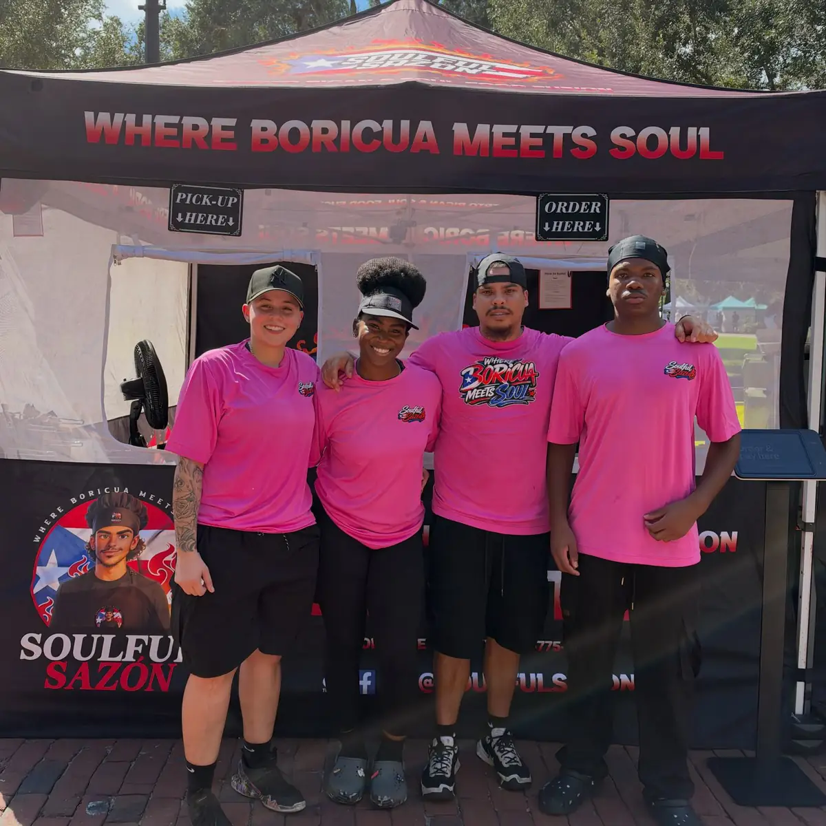 The crew in pink shirts in front of the black Soulful Sazón tent at Lake Eola.