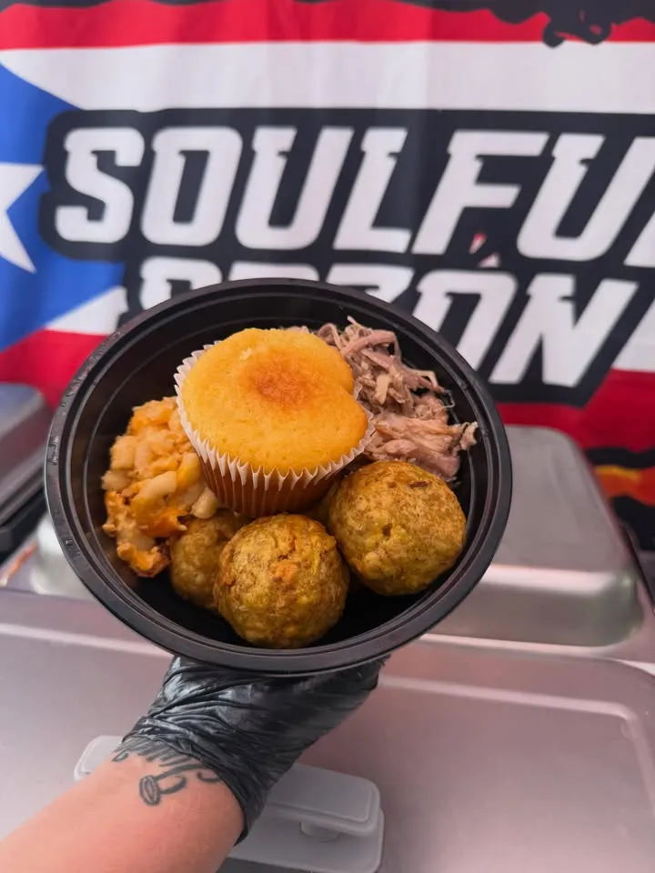 A bowl with cornbread, fried balls and pulled meat in front of the Soulful Sazón banner.