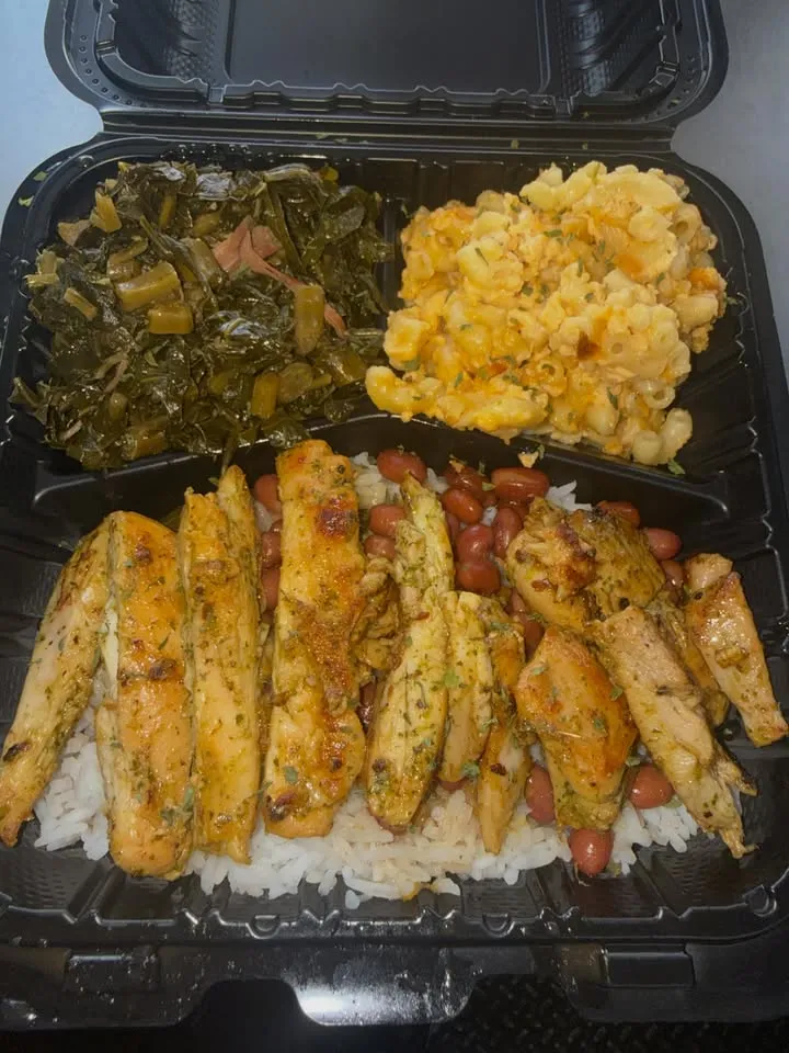 A takeout box with grilled chicken strips over rice, collard greens and mac and cheese.