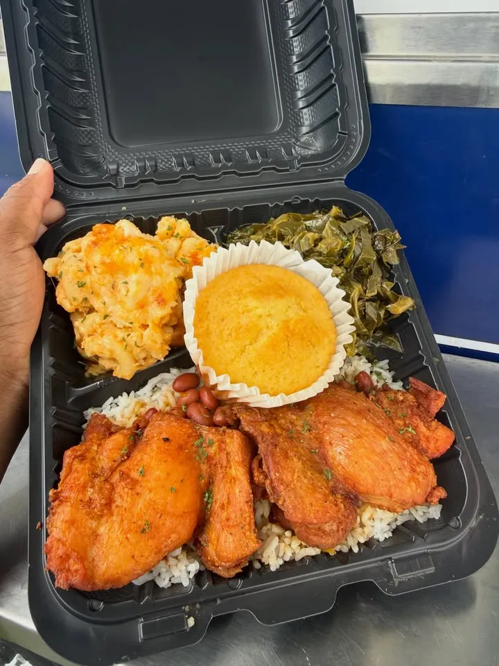 A takeout box with chicken, mac and cheese, greens and a cornbread muffin.