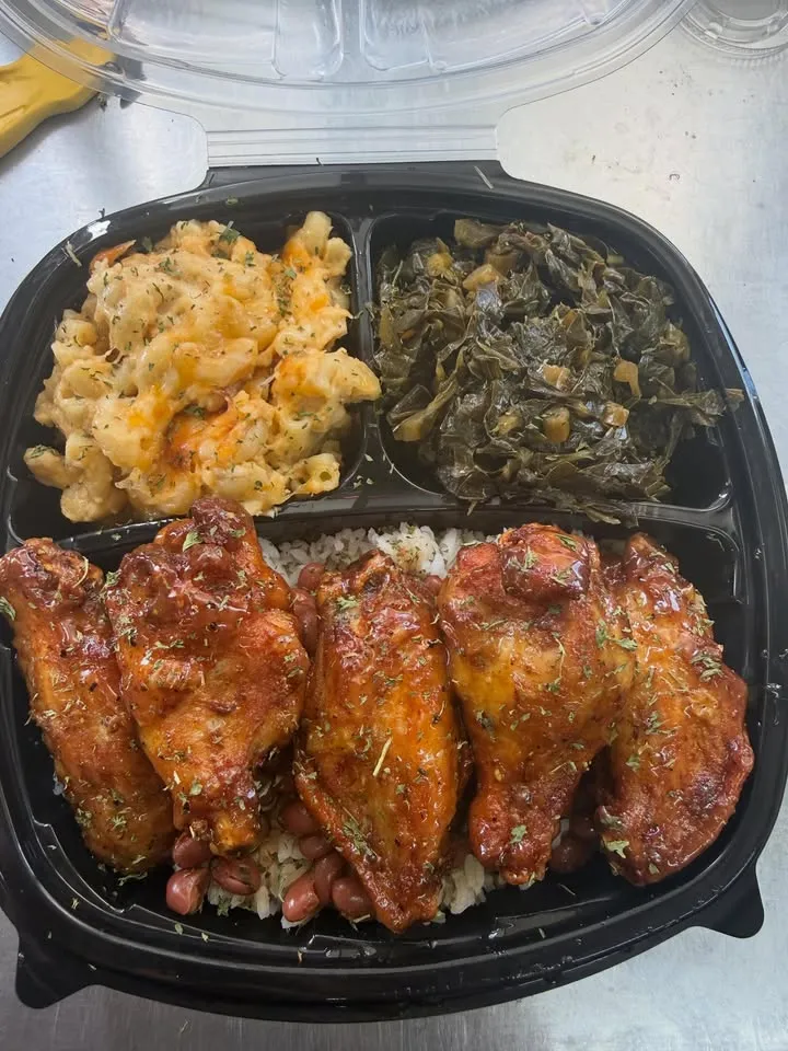 A takeout box with glazed wings over rice, with mac and cheese and collard greens.