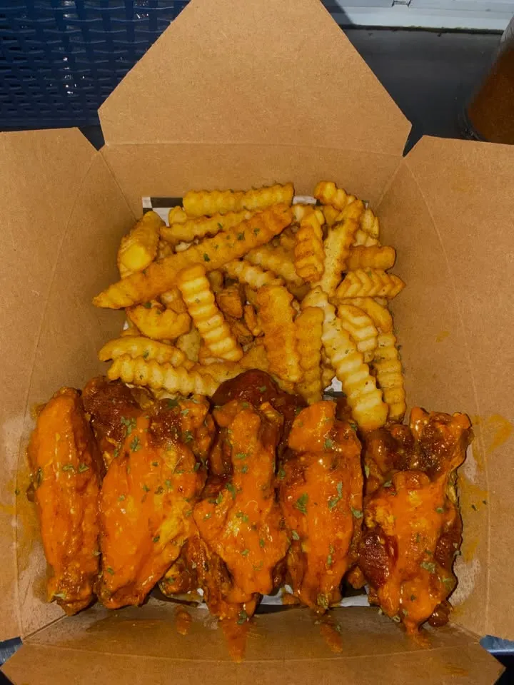 A cardboard box of glazed wings on top of crinkle-cut fries.